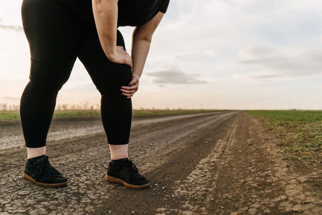 Женщина с избыточным весом трогает боль в ноге