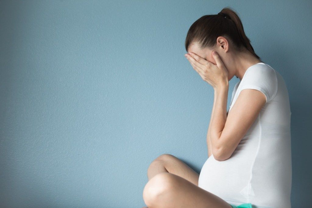 妊娠中の女性は青い背景に座っている間、手で顔を保持し、夫は妊娠中に去った