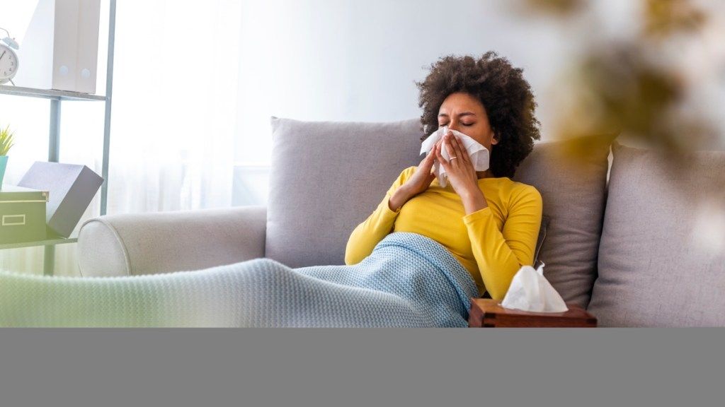 Femeie pe canapea care sufla nasul bolnav acasă