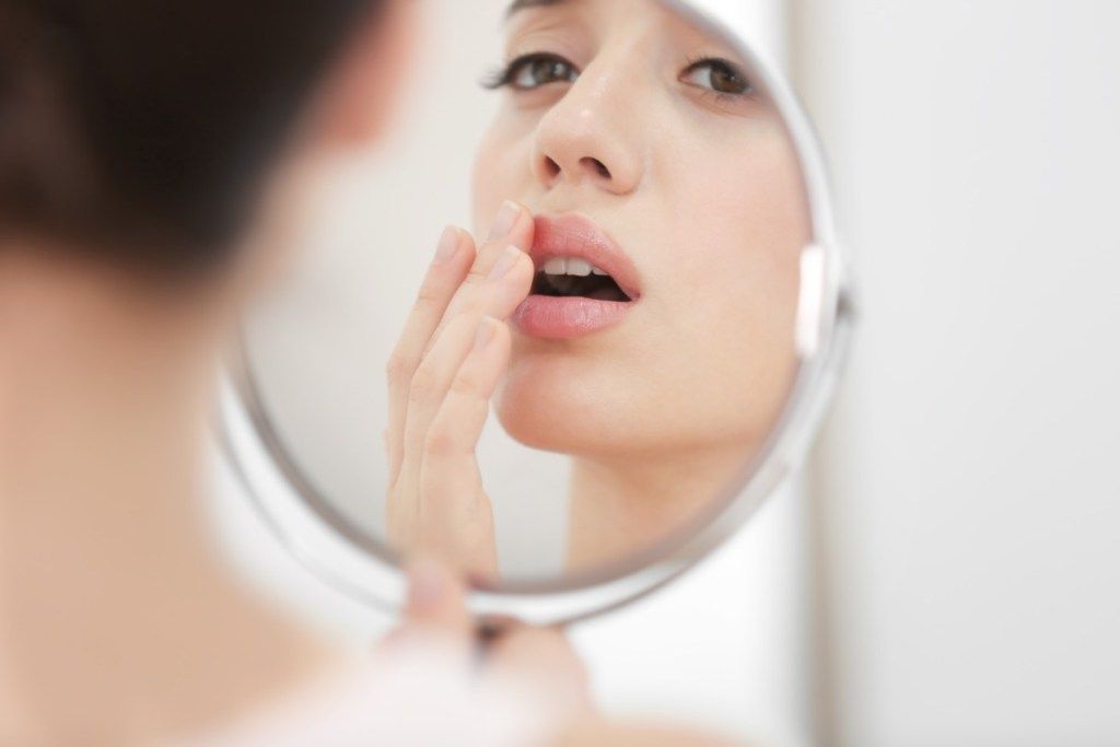 Mujer joven con herpes labial mirando en el espejo en casa
