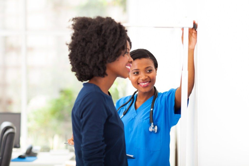 Một y tá da đen đo chiều cao của một nữ bệnh nhân da đen để xem cô ấy cao bao nhiêu