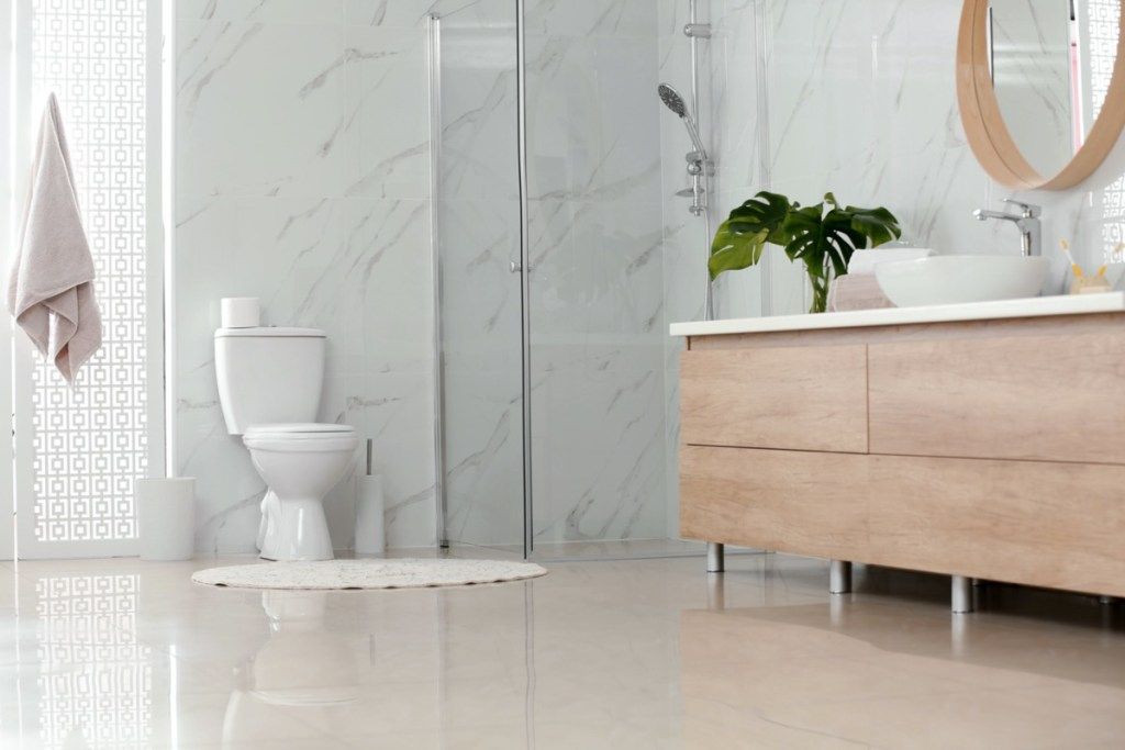 phòng tắm hiện đại với tường đá cẩm thạch nhà vệ sinh màu trắng và đồ nội thất bằng gỗ sáng màu