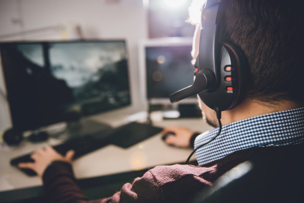Vīrietis, valkājot videospēļu austiņas un spēlējot videospēles savā datorā