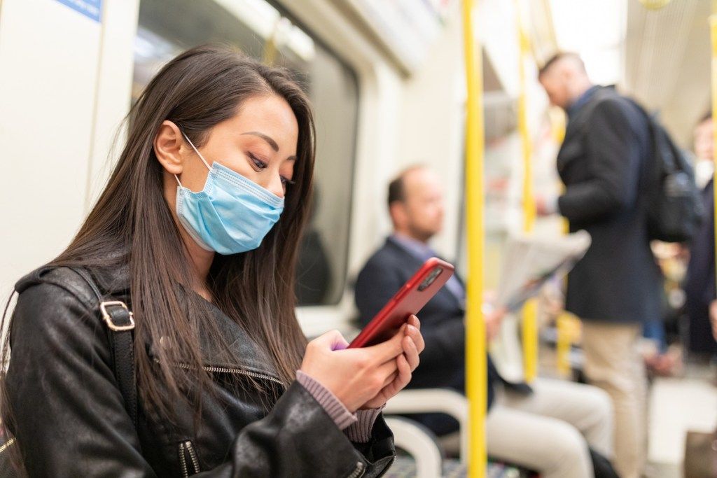 Koronavirüsten korunmak için tüple seyahat ederken yüz maskesi takan genç kadın