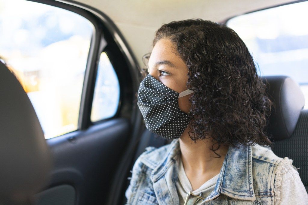 En ung kvinna som bär en ansiktsmask i baksätet på en bil