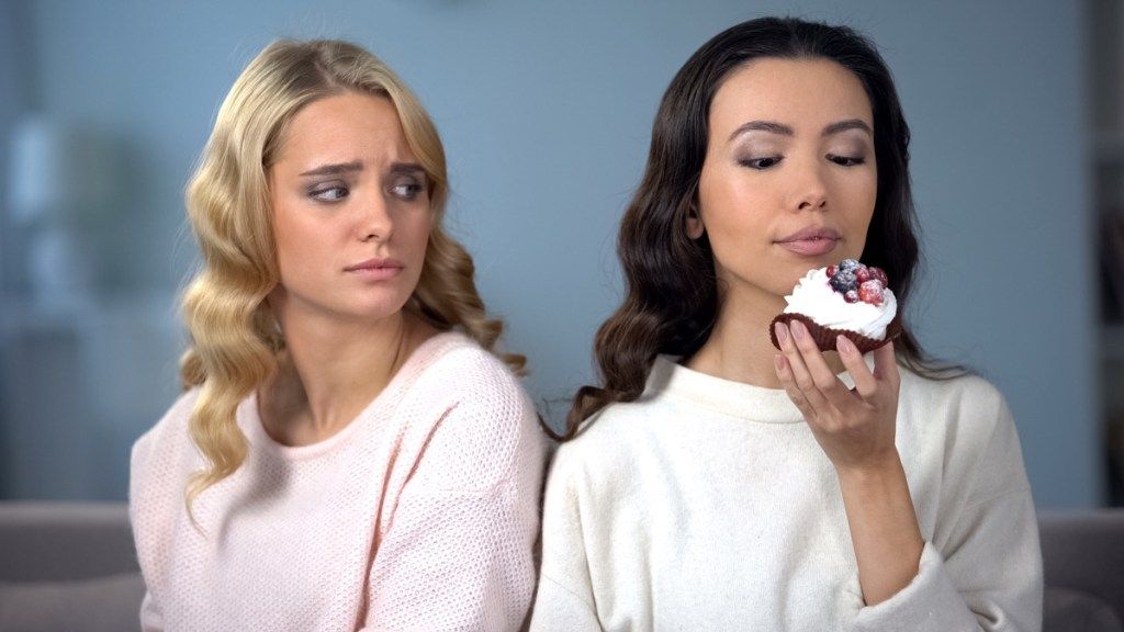 Vrouw jaloers op haar magere vriend die een cupcake eet