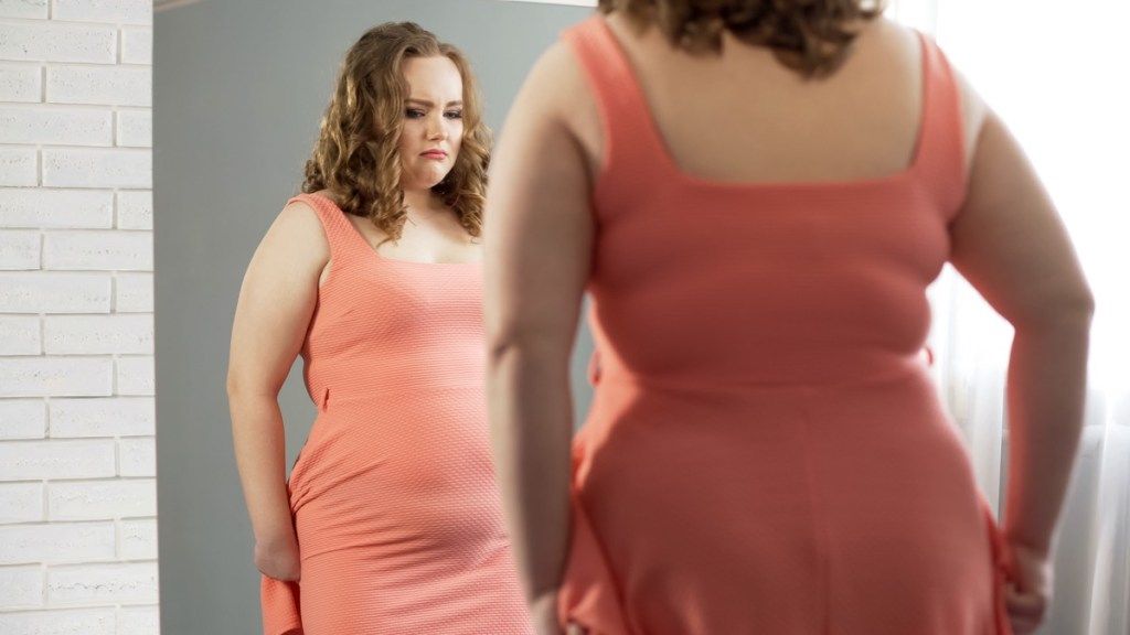 Žena kritizuje své tělo a váhu v zrcadle