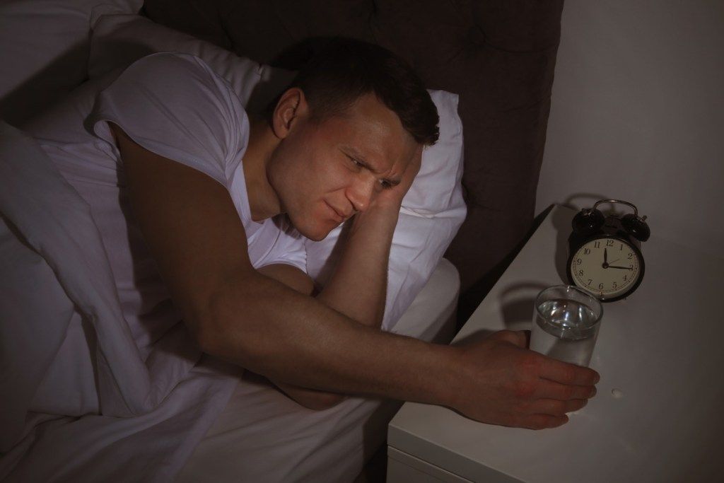 Un bărbat alb de 30 de ani care caută un pahar de apă în pat