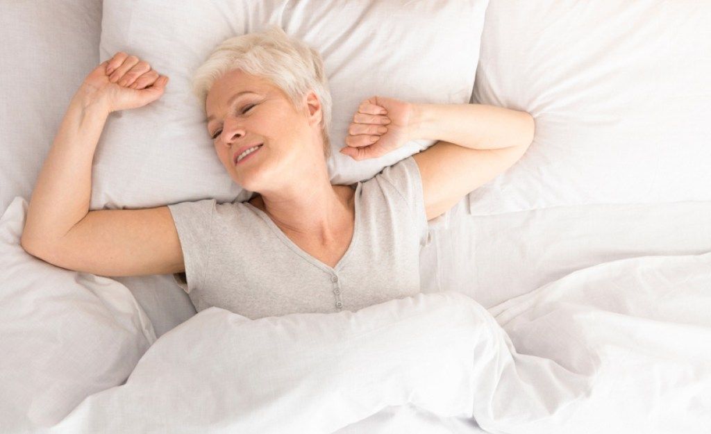 vecākā baltā sieviete pamostas laikā stiepjas gultā