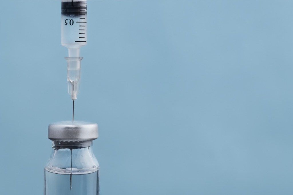 青い背景のワクチンのバイアルに浸した注射器