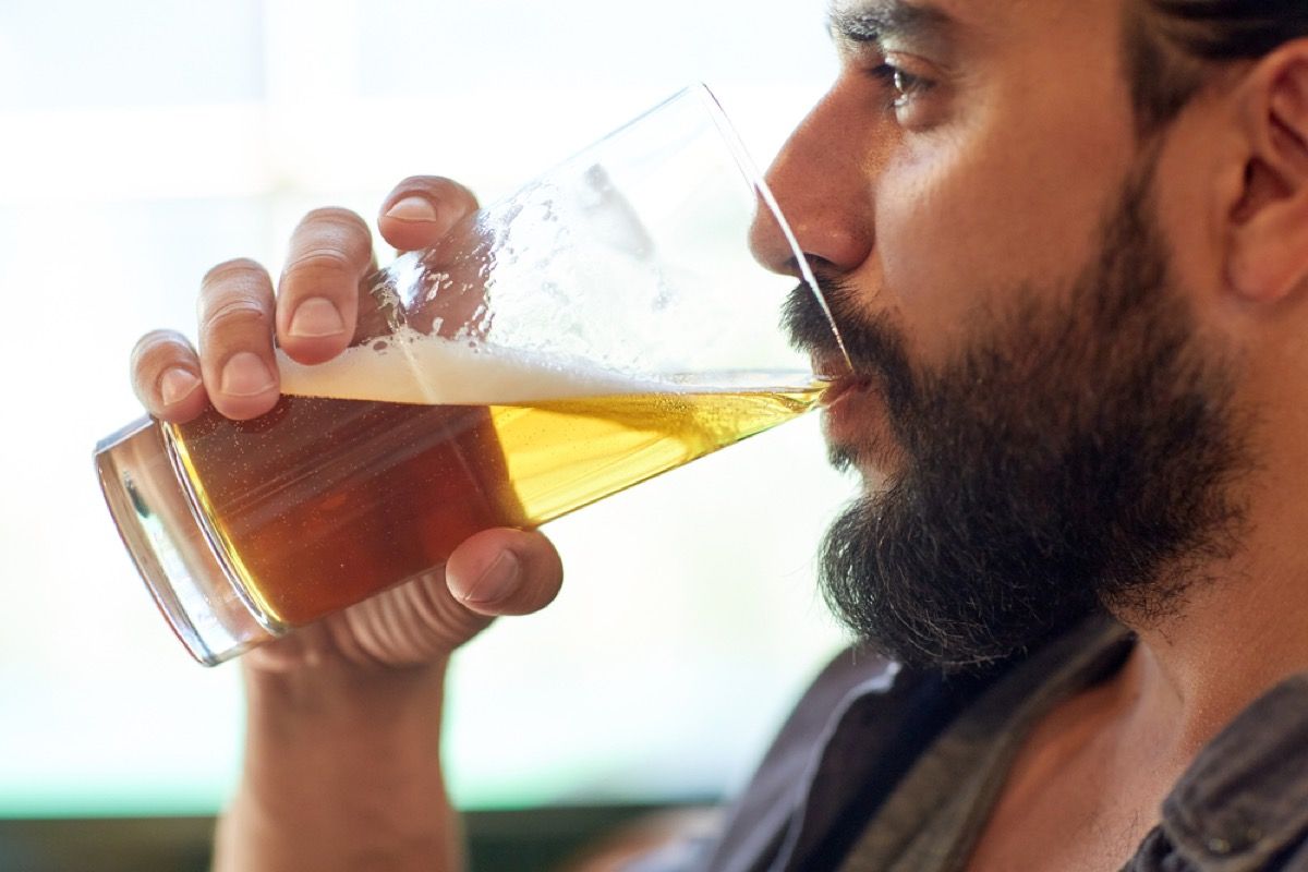 close-up de um homem branco barbudo bebendo um copo de cerveja