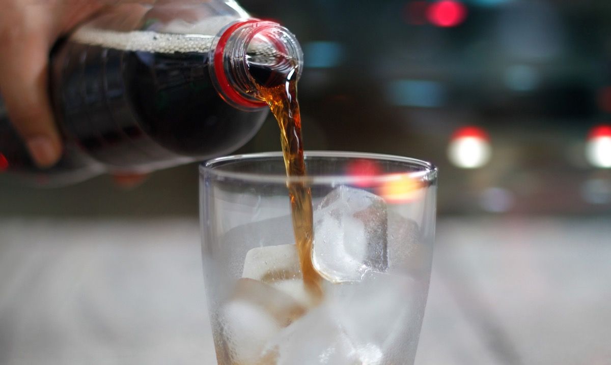 Close up of cola étant versé dans un verre rempli de glace