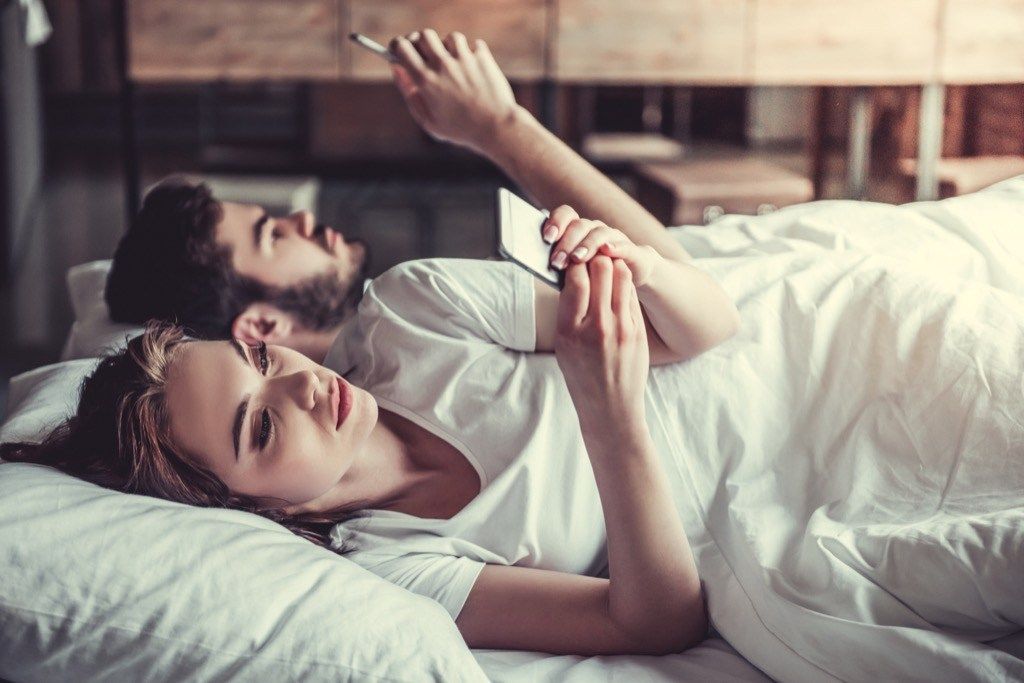 uttråkat par som ligger i sängen med smartphones, saker du aldrig ska säga till din make