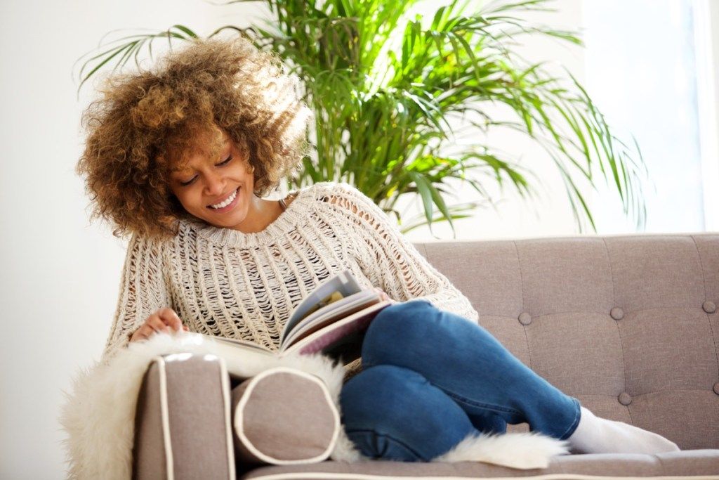 Retrato de uma atraente mulher afro-americana sentada no sofá lendo um livro