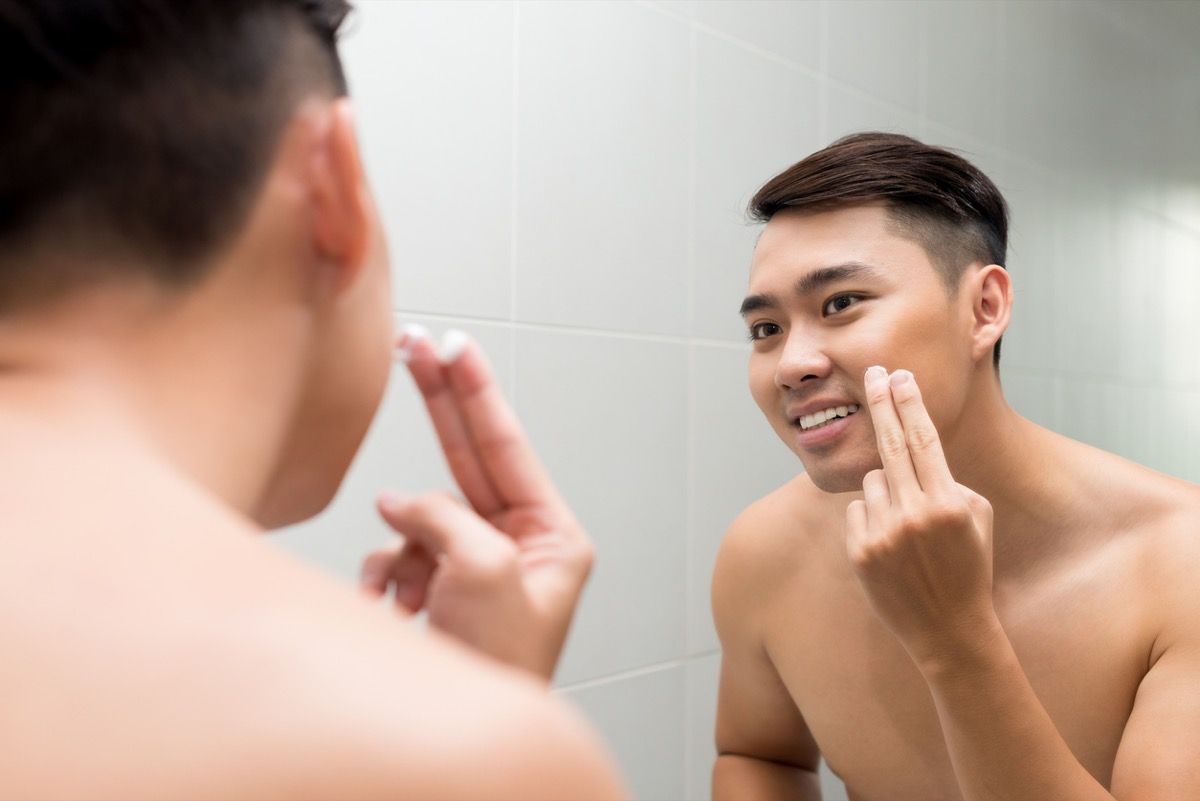 Tânăr asiatic care aplică loțiune facială în fața oglinzii