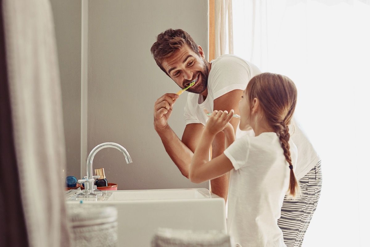 Pai feliz e filha escovando os dentes no banheiro