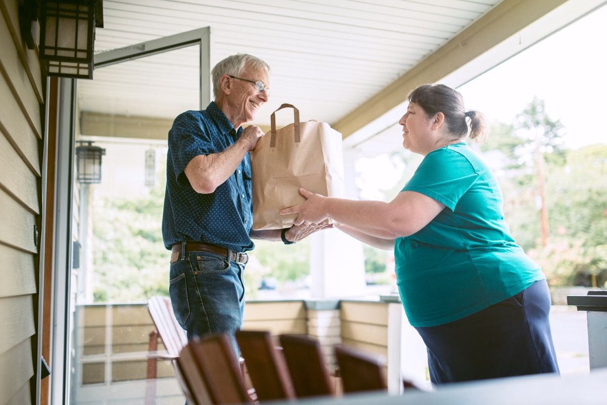 Egy kedves és gondos szomszéd vagy barát friss termékeket szállít az élelmiszerboltból egy idős férfinak otthonában.
