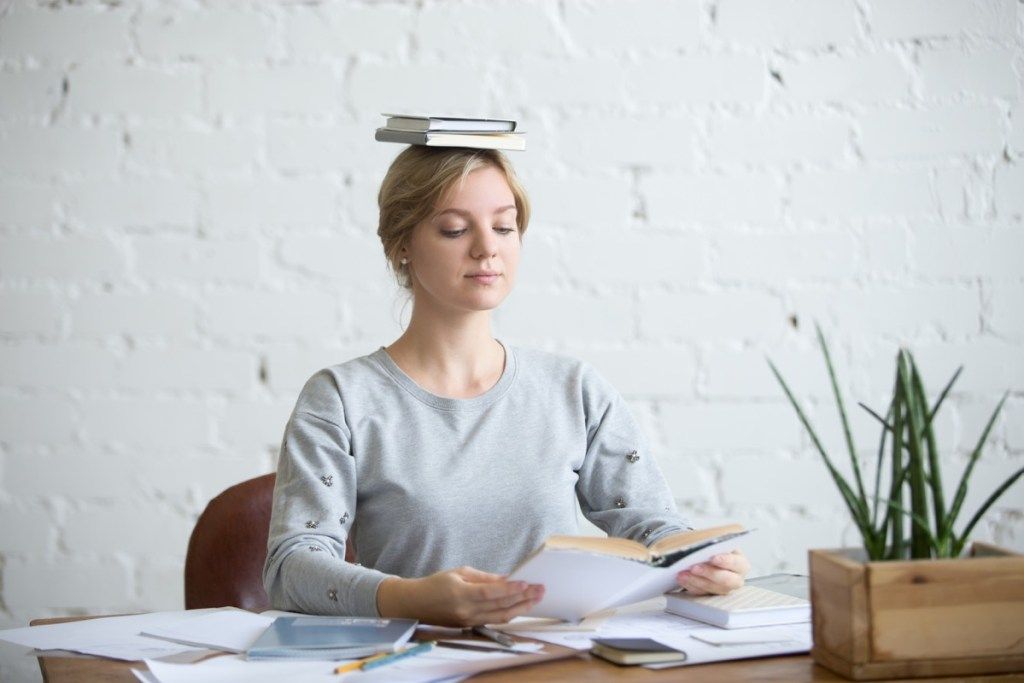 डेस्क पर आकर्षक महिला का चित्र, उसके सिर पर किताबें