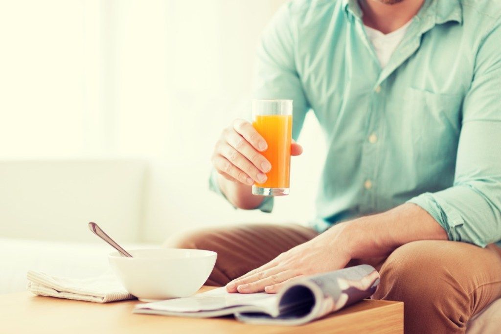 ผู้ชายกำลังดื่มน้ำผลไม้ขณะอ่านกระดาษและกินอาหารเช้า