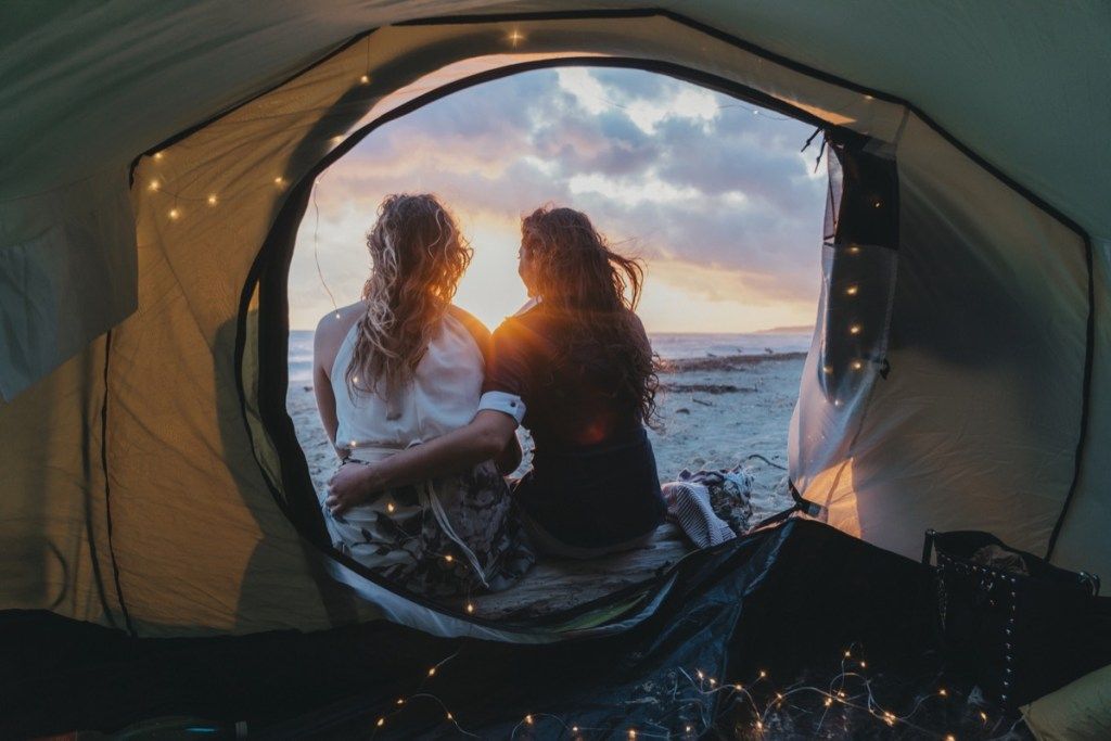 Jauns pieaugušais lesbiešu pāris apbrīno saulrietu teltī pludmalē atvaļinājumā