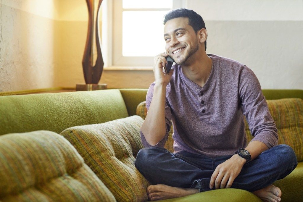 צעיר משוחח בשמחה בטלפון על הספה