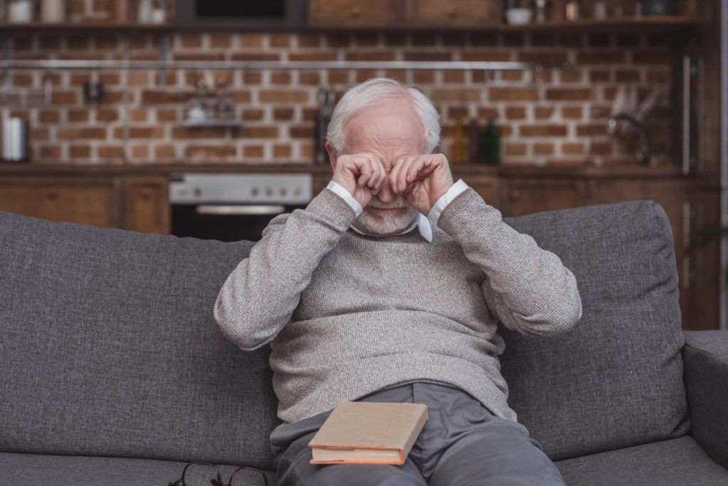 äldre vit man gnuggar ögonen på soffan