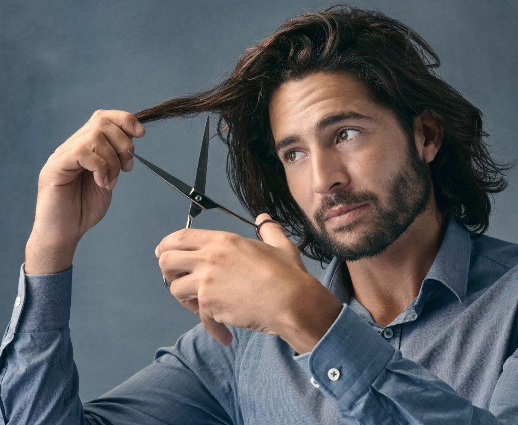 Foto de estudio de un apuesto joven cortándose el pelo contra un fondo gris