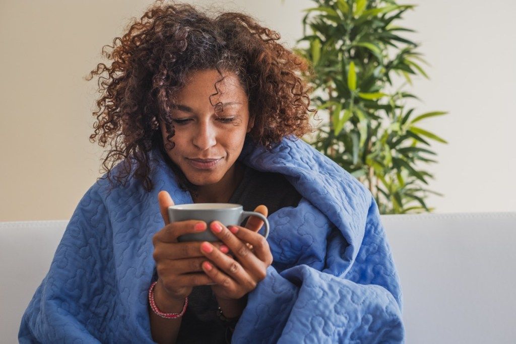 Студена жена, загряваща се с чаша кафе и одеяло
