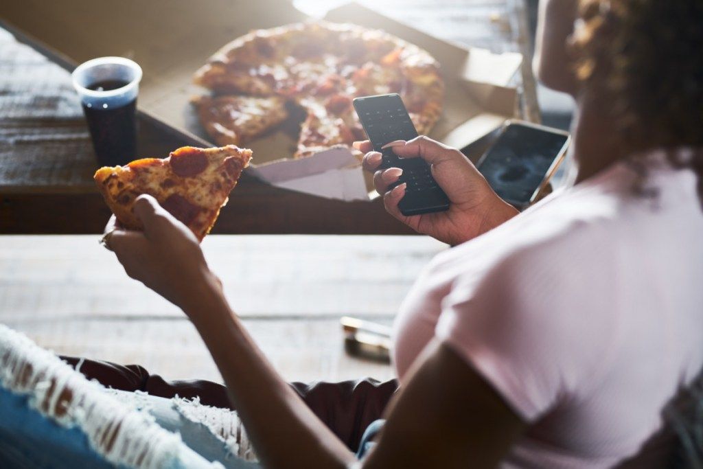 femeie stând târziu, relaxându-se acasă uitându-se la televizor și mâncând pizza