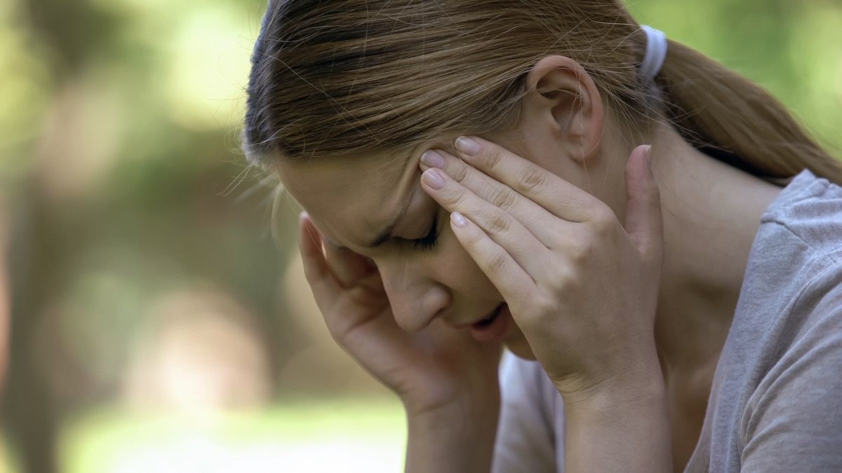 Mujer joven que sufre dolor de cabeza agudo, preocupándose por los fracasos, día estresante