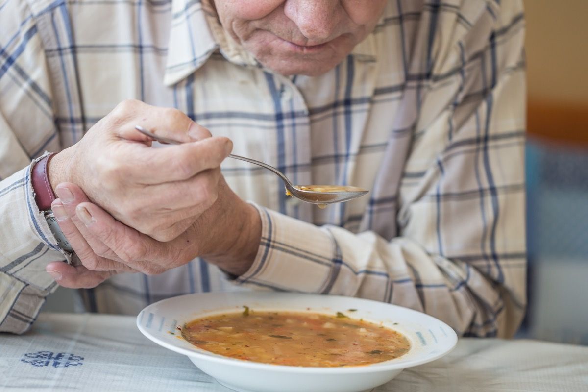 Človek s tresenjem, ki še vedno drži roko, da bi jedel juho