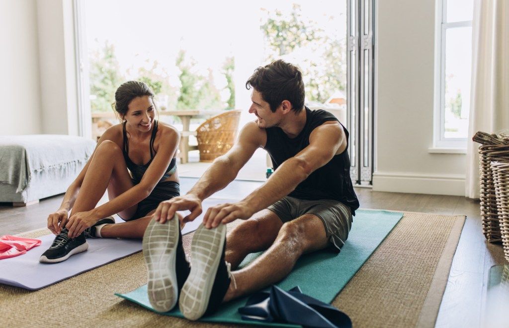 Un tânăr cuplu care se exercită împreună pe covorașe de yoga în sufrageria lor.
