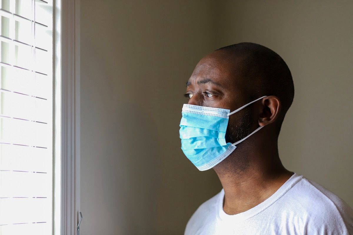 Pencereden dışarı bakarken virüs bulaşmasını önlemek için koruyucu yüz maskesi takan Afrikalı-Amerikalı bir adam