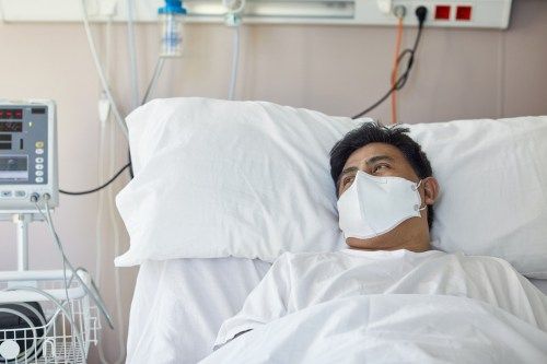 Портрет на пациент от мъжки пол в началото на 40-те, гледайки далеч от камерата, докато лежи в болничното легло, носещ защитна маска за лице и се възстановява от коронавирус
