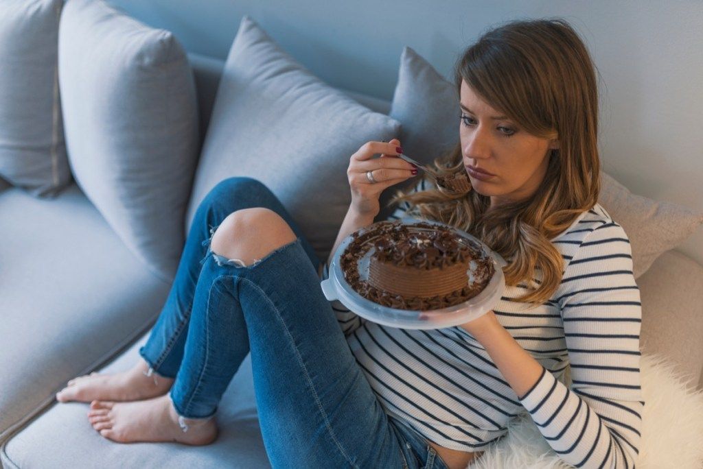 چاکلیٹ کیک کے ساتھ صوفے پر اپنے احساسات کھا رہی اداس لڑکی