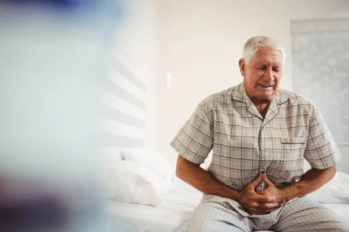   Hombre mayor enfermo que sufre de dolor de estómago sosteniendo su estómago en el dormitorio