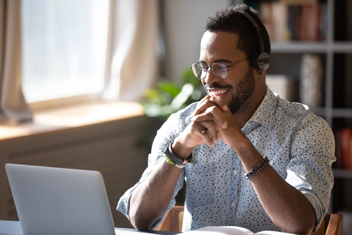 ung sort mand smilende og chatter på sin bærbare computer