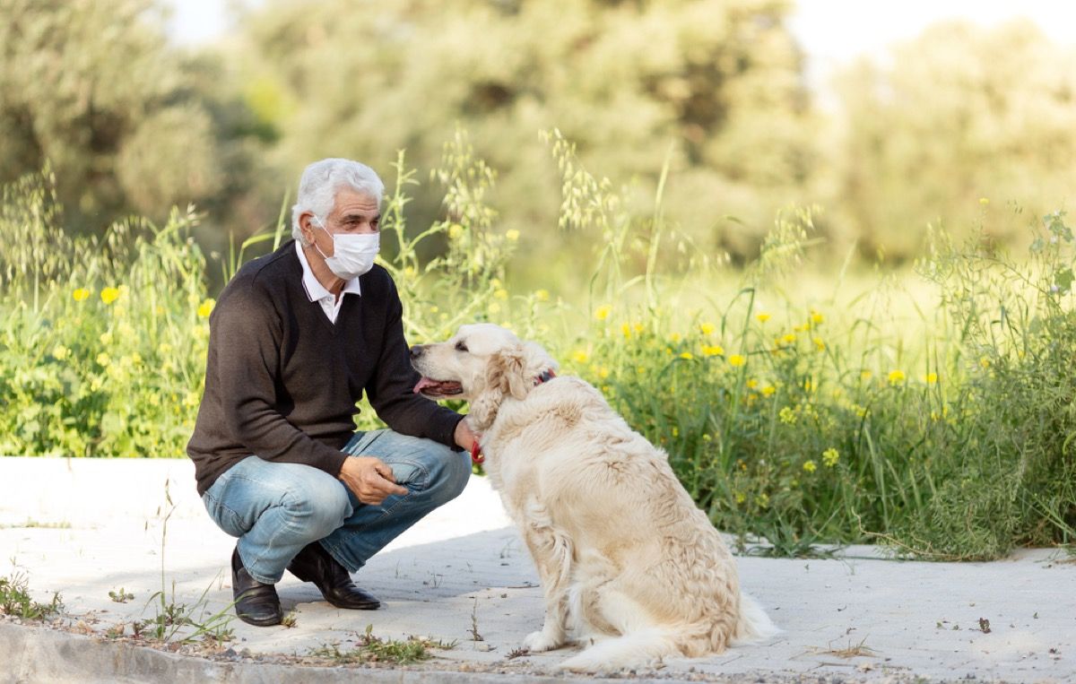 bărbat alb mai în vârstă cu o mască de față ghemuit lângă câinele său afară