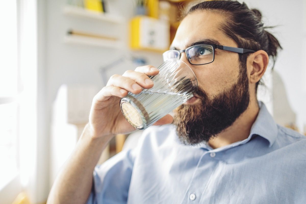 Човек са мужицом и чашама пије воду код куће