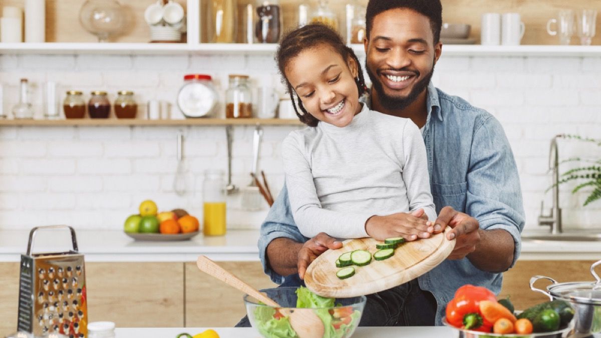 fekete apa segít lányának nyomja uborkát egy salátástálba