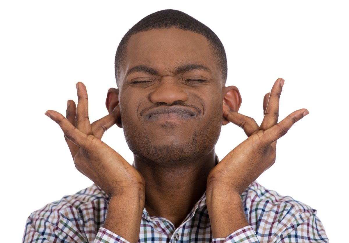 Schwarzer Mann legt Finger in seine Ohren, weil er nicht zuhören will, überprüfen Sie das Hören, um ein gesünderer Mann zu sein