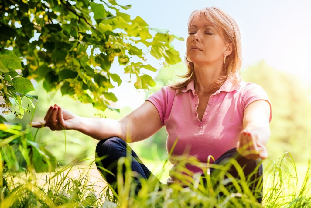 възрастна жена, медитираща в трева, начини, по които тялото ви се променя след 40 години
