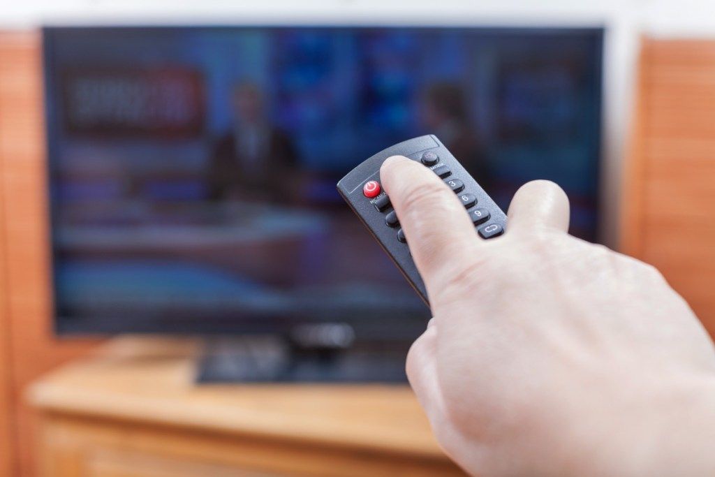 Taong gumagamit ng isang remote sa telebisyon upang patayin ang kanilang TV