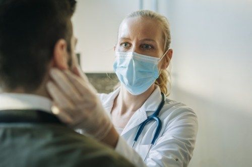 Arts die chirurgisch masker draagt ​​dat besmette patiënt onderzoekt. Rijpe gezondheidswerker die medio volwassen mens controleert. Ze zijn bij de apotheek.