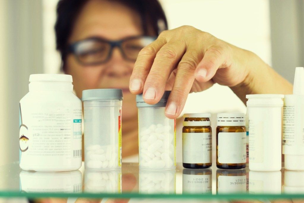 kvinna som tittar igenom sina mediciner i hennes medicinskåp, hälsofrågor efter 50