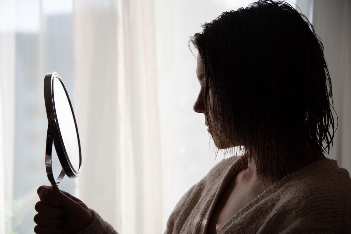 Žena koja gleda svoje obrve u ručno zrcalo