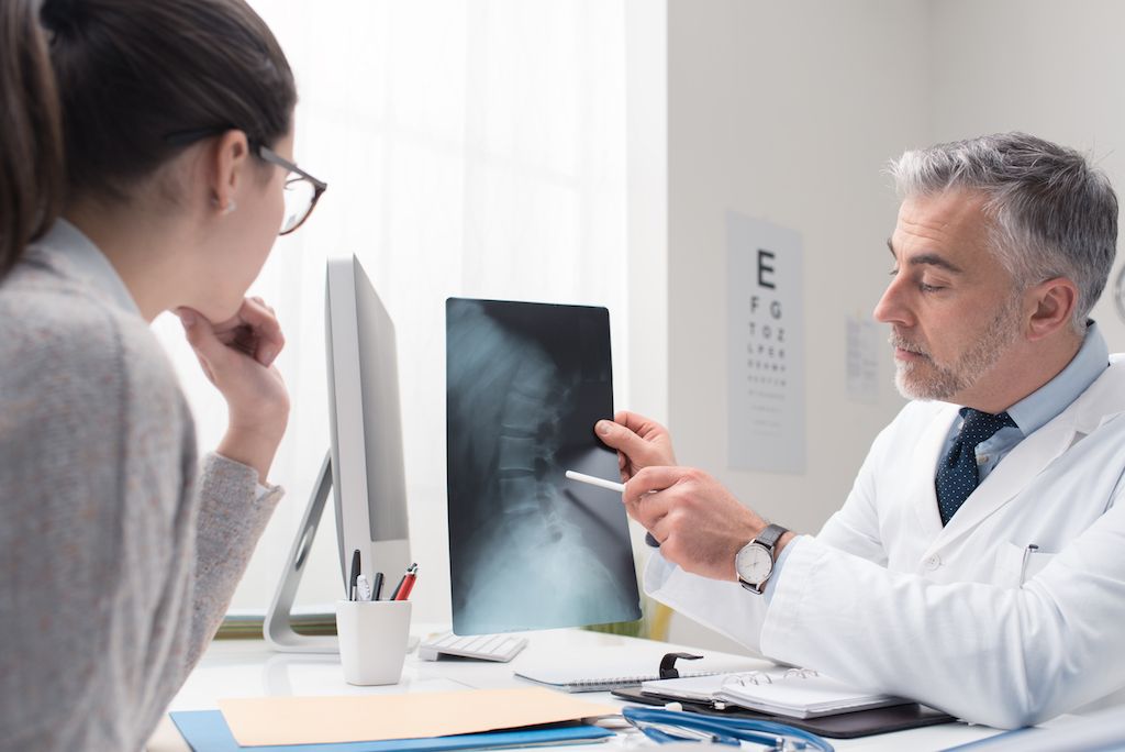 Frau und Arzt betrachten eine Röntgenaufnahme einer Wirbelsäulenverletzung