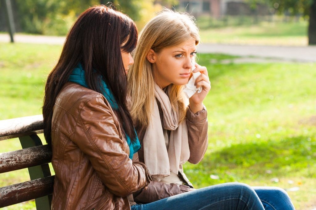 женщина утешает плачущего друга на скамейке
