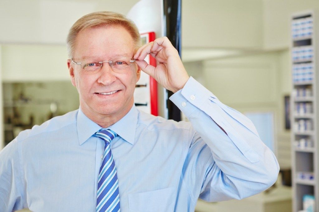 vecāks vīrietis ar jaunām brillēm pie acu ārsta, jautājumi par veselību ir vecāki par 40 gadiem