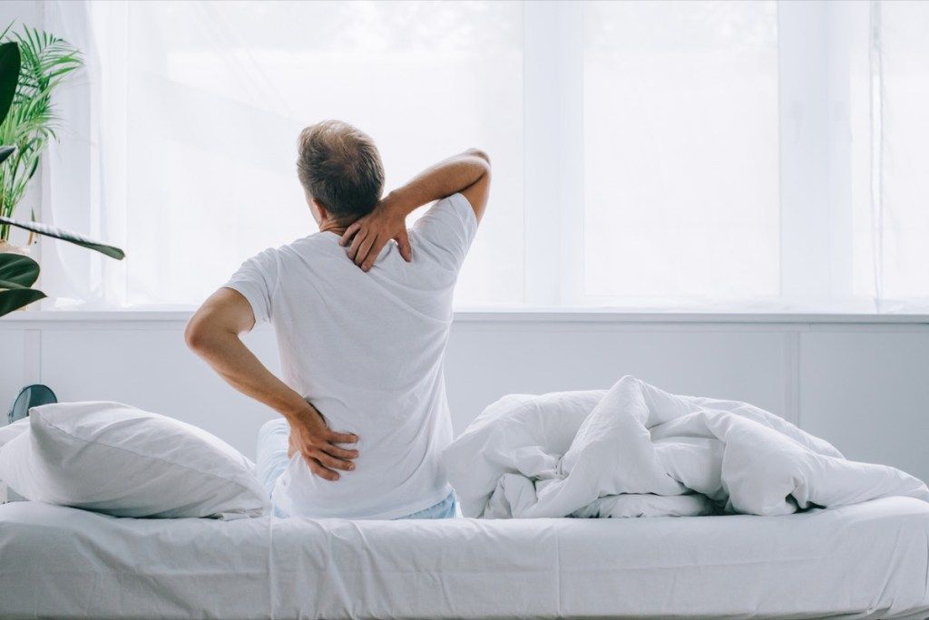 moški z bolečinami v hrbtu, ki sedi na postelji